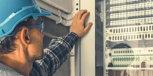 Man observes machinery with an ipad in hand, wearing a construction hat and vest on the left hand side of the image. 